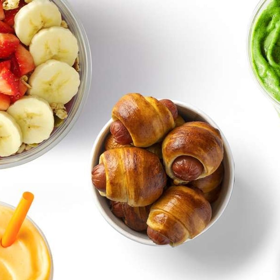 A vibrant flat lay of Jamba menu items including a smoothie bowl, green smoothie, orange smoothie, pretzel bites, and churro bites.