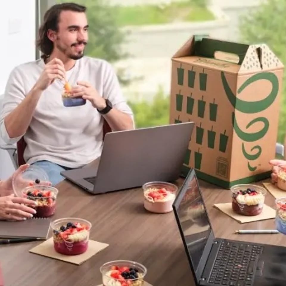 Four people enjoying Jamba smoothie bowls at a table with laptops and a Jamba catering box.
