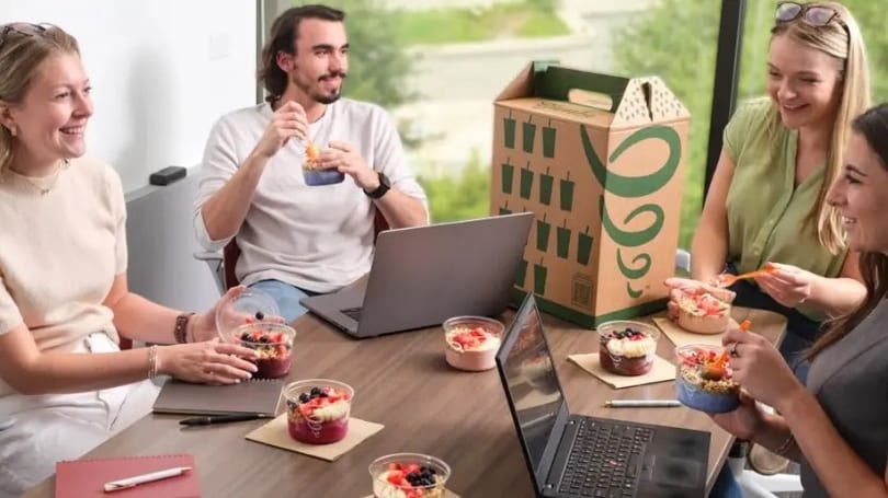 Four people enjoying Jamba smoothie bowls at a table with laptops and a Jamba catering box.