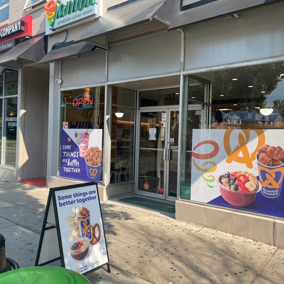 The exterior of an Auntie Anne's and Jamba Juice storefront with promotional window clings and an A-frame sign.