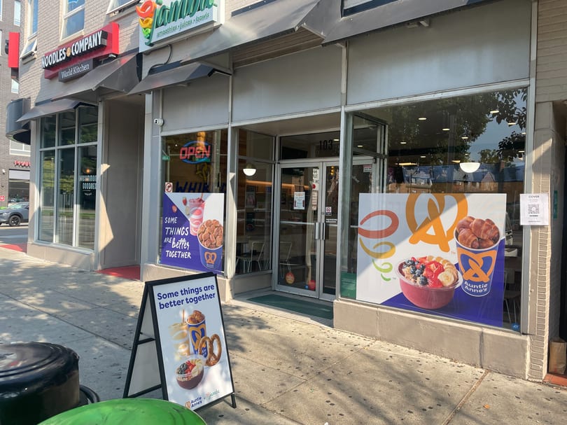 The exterior of an Auntie Anne's and Jamba Juice storefront with promotional window clings and an A-frame sign.